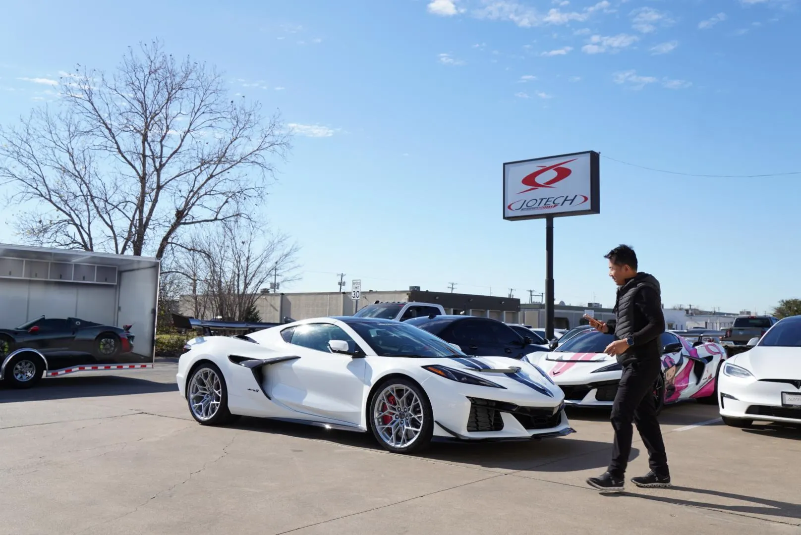 White C8 Corvette Z06 parked outside Jotech Motorsports with other performance cars and a man walking by.