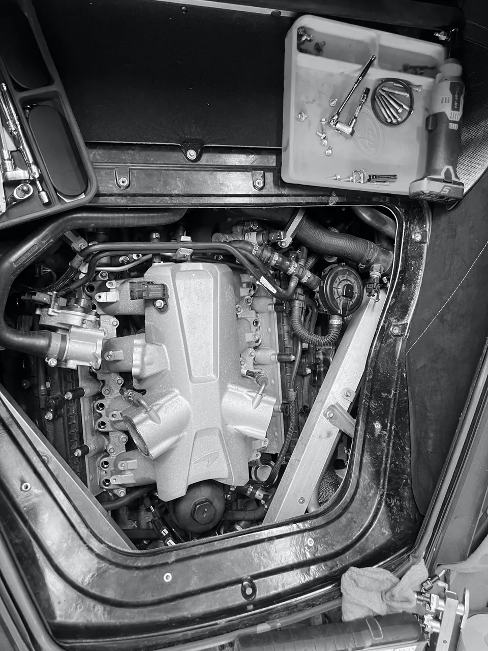 A McLaren engine bay undergoing maintenance or modification, with an intake manifold visible and tools laid out.