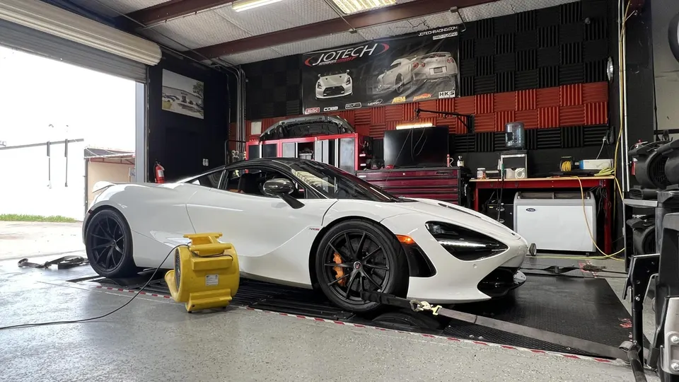 A white McLaren 720S supercar strapped to a dynamometer in a performance tuning shop.