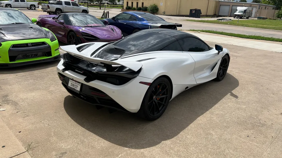 White McLaren 720S, green Nissan GT-R, and other supercars parked outside a performance shop.