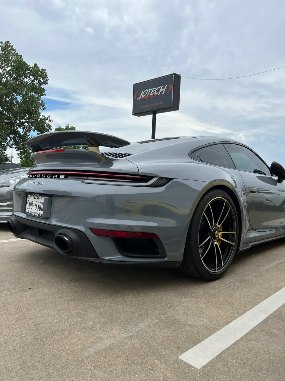 Grey Porsche 911 (992) with a large rear wing and aftermarket exhaust tips parked outside Jotech Motorsports.