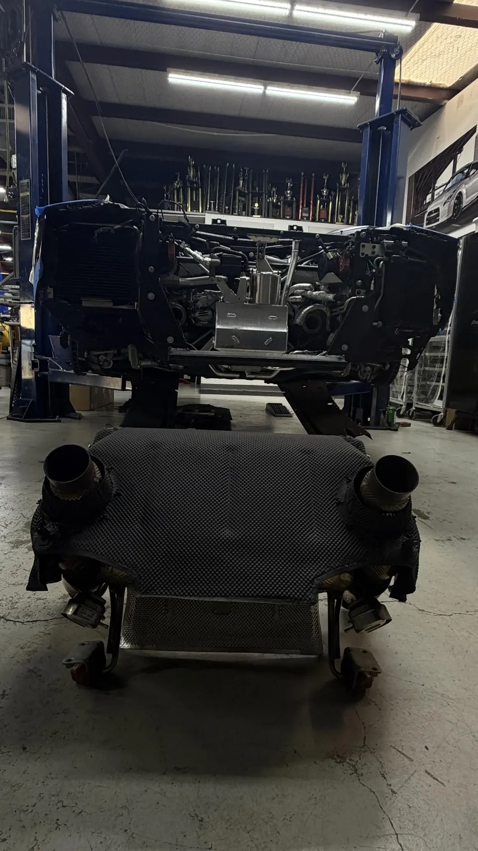 A car on a lift in a performance shop with its exhaust system removed, featuring carbon fiber components.