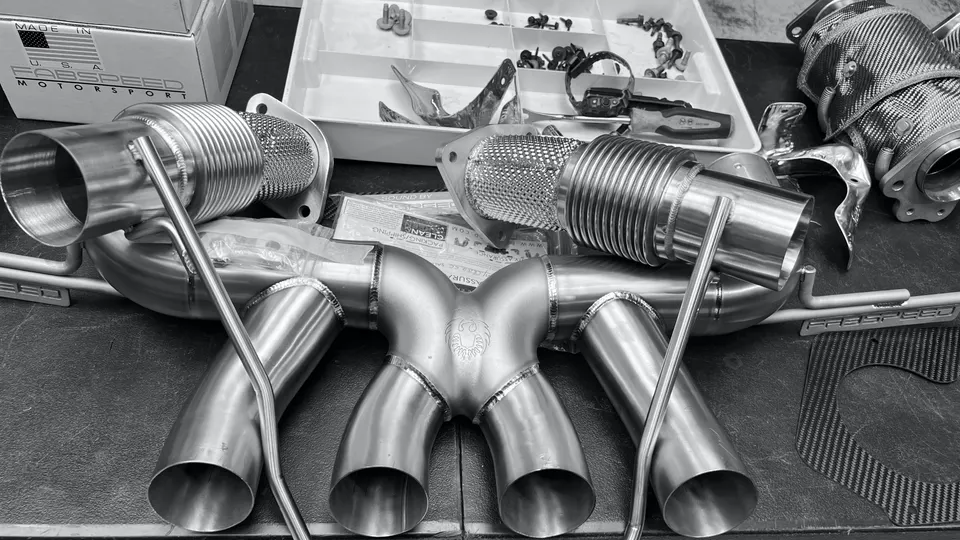 Fabspeed stainless steel performance exhaust system with heat shields and carbon fiber components on a workbench.