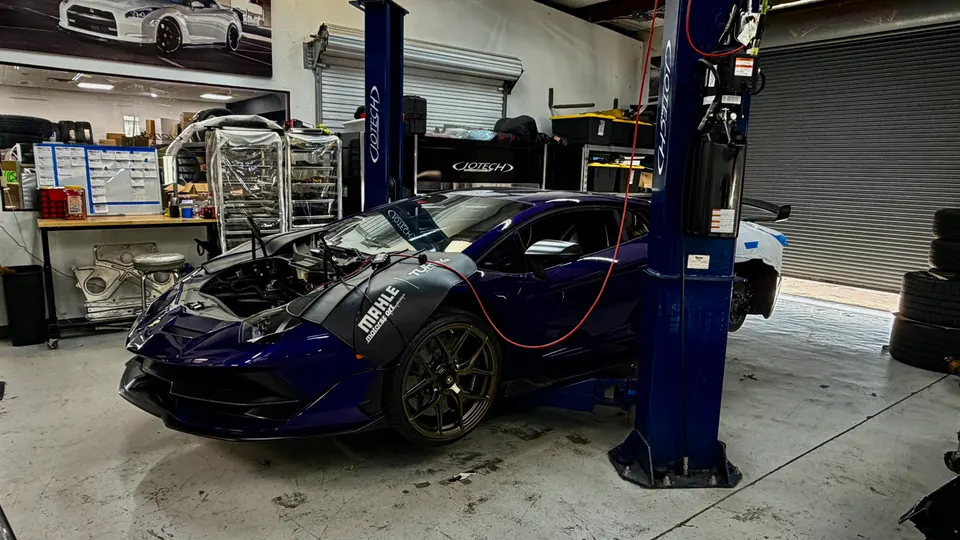 A purple Lamborghini Huracan on a car lift in a performance tuning shop with its hood open for service.