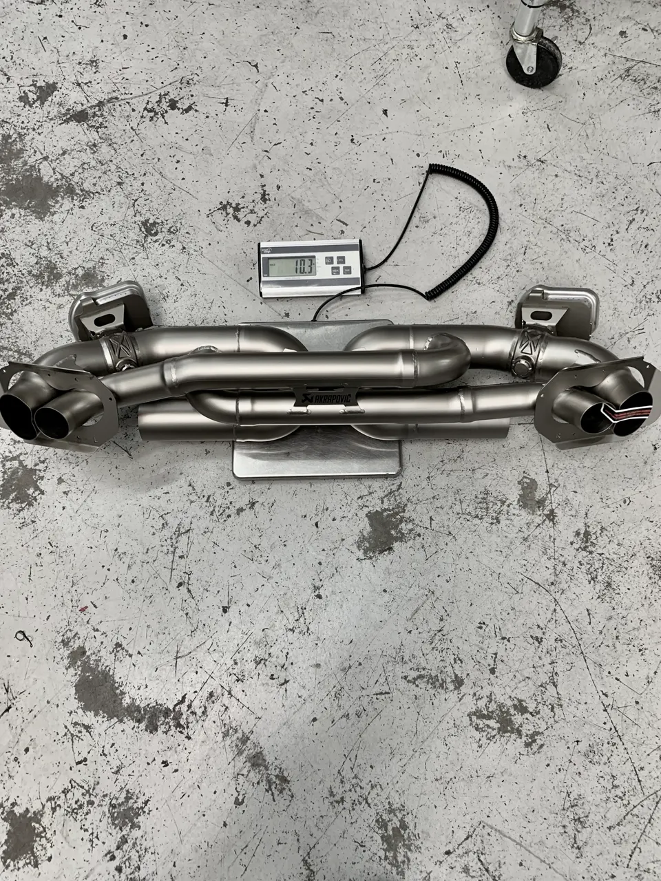 Akrapovic titanium exhaust system on a scale, showing a weight of 10.3 on the digital display.