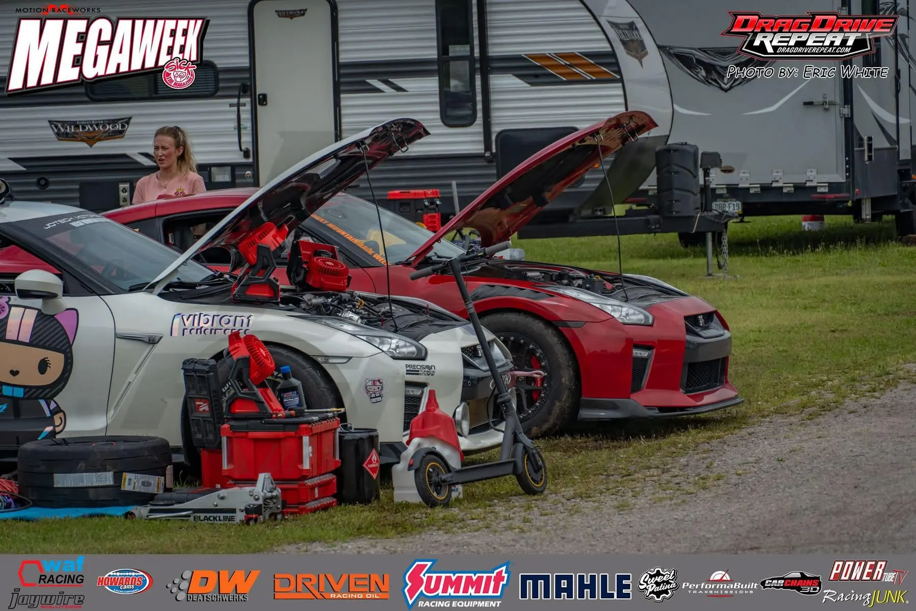 Two Nissan GT-R drag cars with open hoods in a pit area at a Megaweek drag racing event, surrounded by tools and equipment.