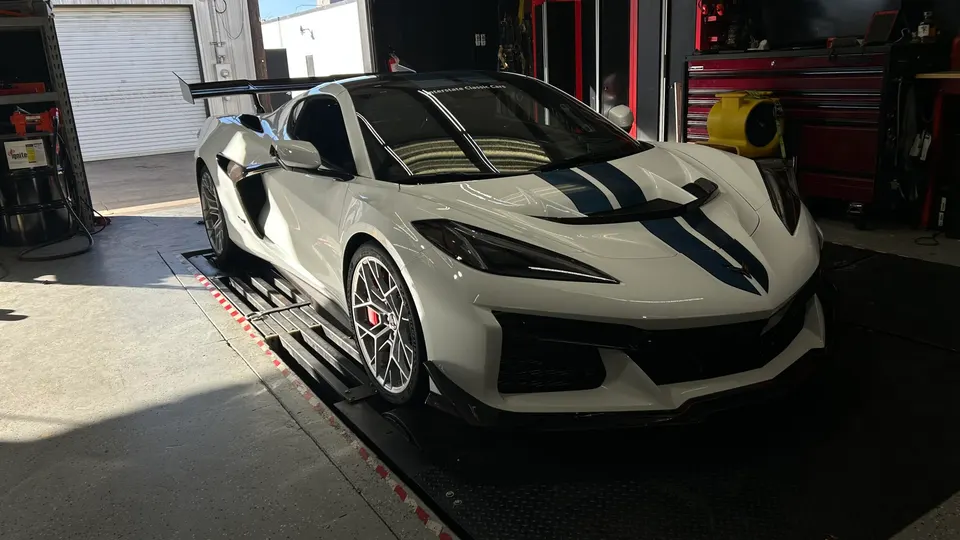 White Corvette C8 Z06 with blue racing stripes on a dynamometer for performance testing.