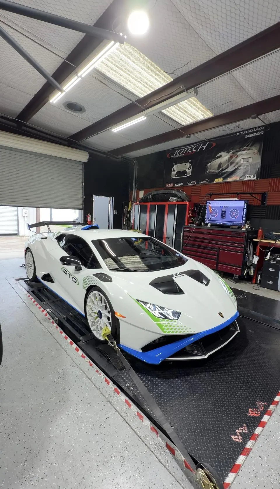 A white Lamborghini Huracan STO strapped to a dyno at Jotech Motorsports for performance tuning.