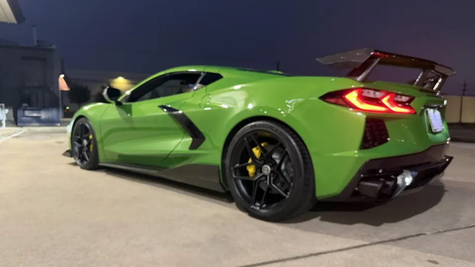 A green C8 Corvette with an aftermarket wing and custom exhaust parked at night.