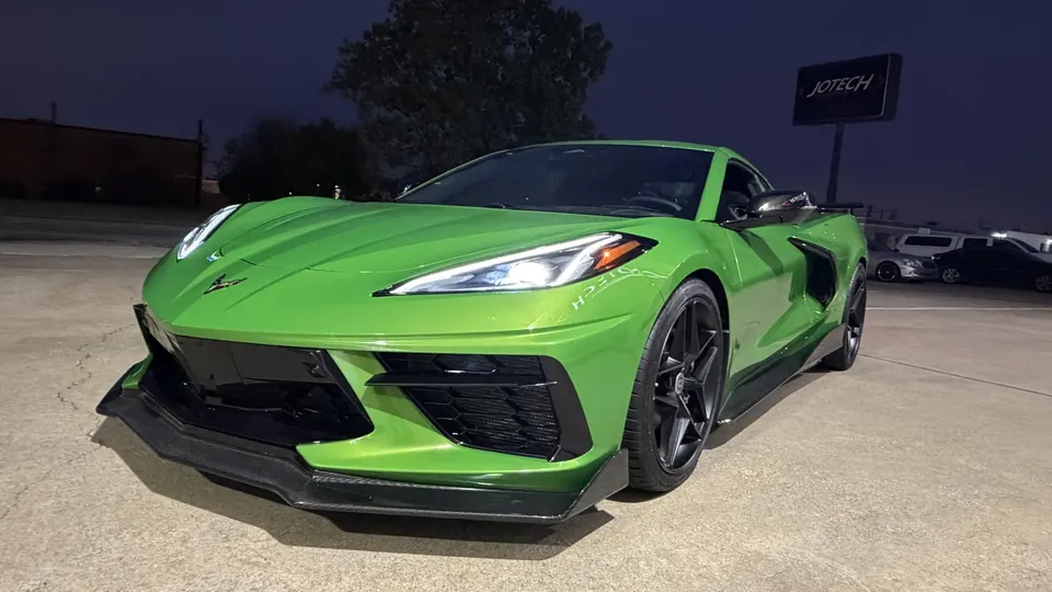 A vibrant green Chevrolet Corvette C8 with an aftermarket front splitter parked at night in front of a Jotech sign.