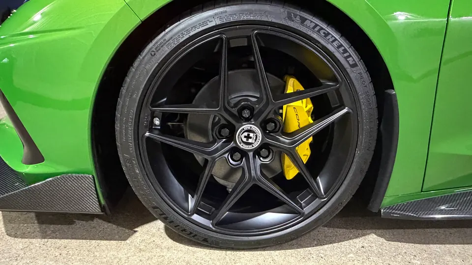 Close-up of a green car's black HRE performance wheel, Michelin tire, and bright yellow brake caliper with carbon fiber trim.