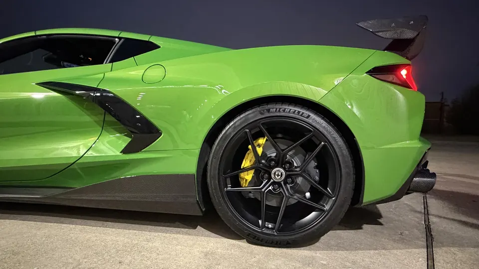 A bright green C8 Corvette with aftermarket black wheels, yellow brake calipers, and a carbon fiber rear wing.