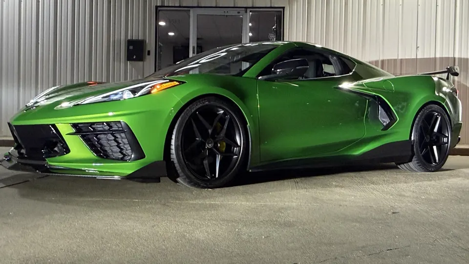 A vibrant green Chevrolet Corvette C8 with aftermarket black wheels, a front splitter, and a rear wing parked outside a building.
