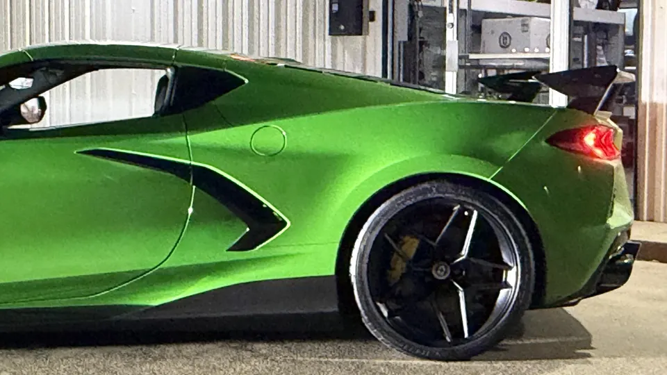 Green C8 Corvette with a large aftermarket rear wing and custom wheels, showcasing exterior aero modifications.