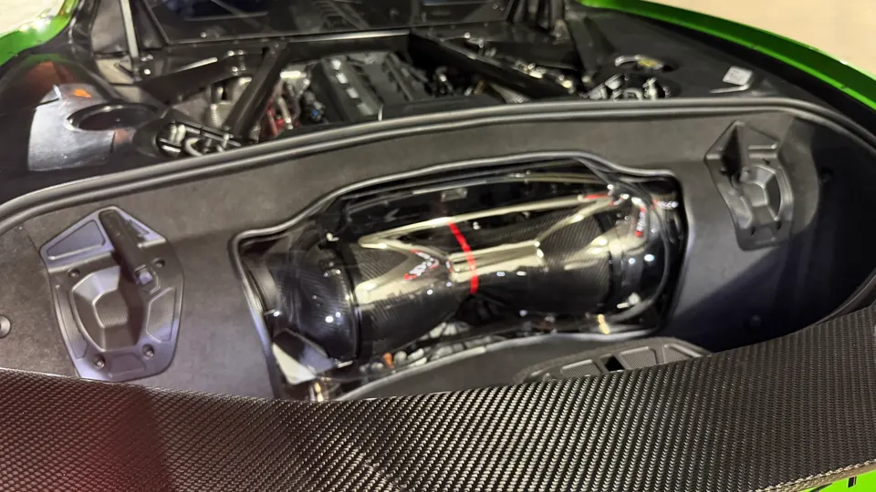 Close-up of a green Corvette C8 engine bay showcasing a carbon fiber induction system.