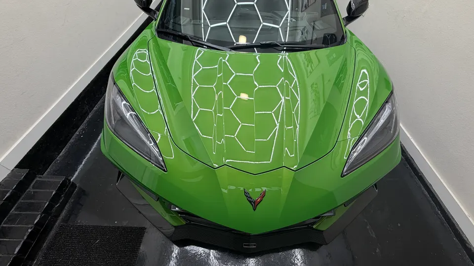 Bright green Chevrolet Corvette C8 front view in a showroom with hexagonal light reflections on the hood.