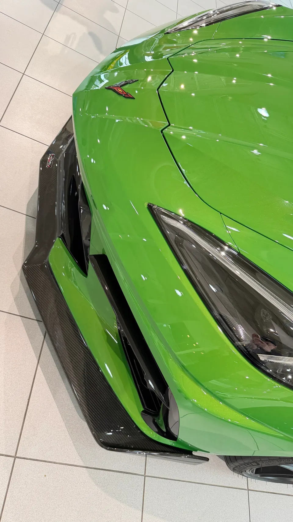 Close-up of the front of a bright green Lamborghini with carbon fiber aero and a sleek headlight.