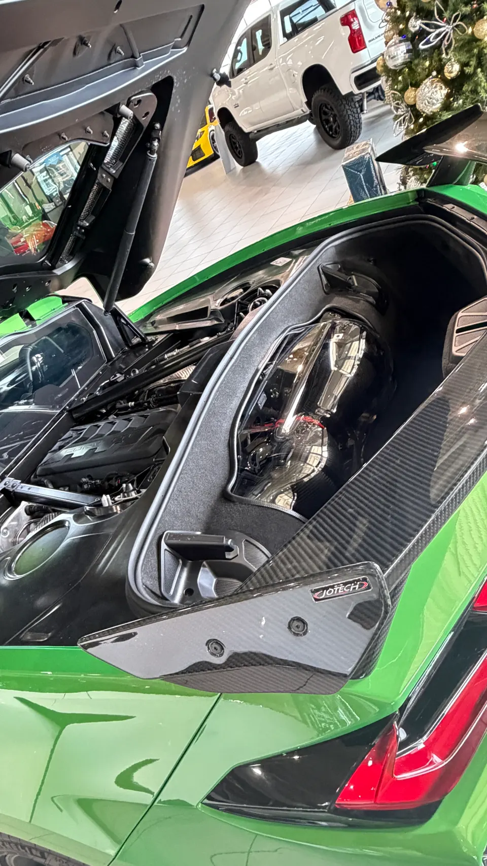 A green C8 Corvette with its engine bay open, showcasing the engine and a Jotech carbon fiber induction component.