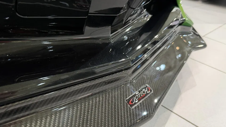 Close-up of a black car's carbon fiber side skirt with a Jotech logo, showcasing exterior aerodynamic details.