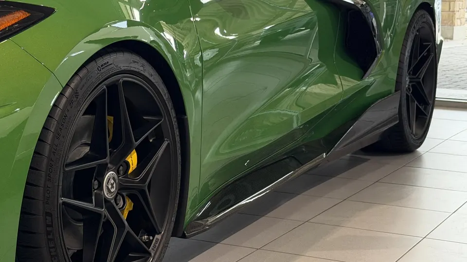 A green Corvette C8 with HRE wheels, Michelin tires, yellow brake calipers, and a carbon fiber side skirt.