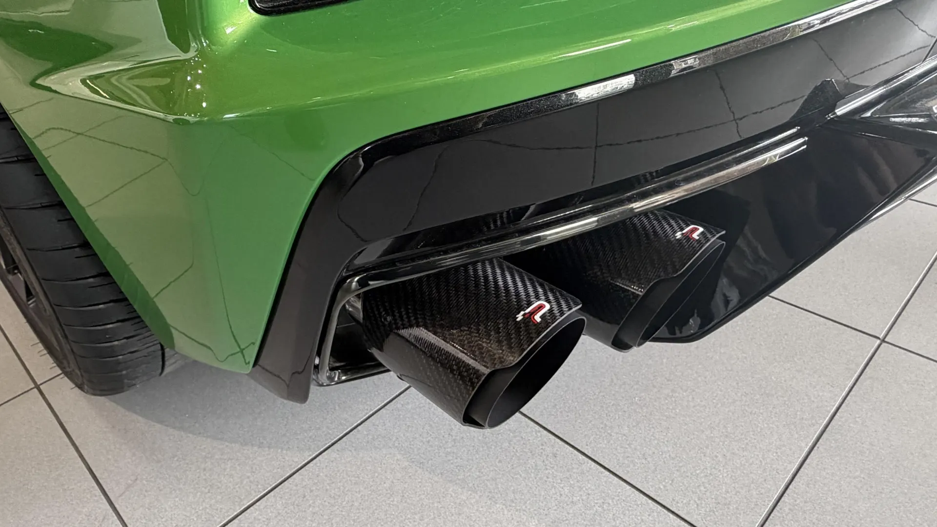 Close-up of a green car's rear bumper featuring carbon fiber exhaust tips and a black diffuser.
