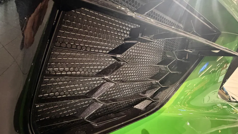 Close-up of a green Lamborghini's front bumper grille with a honeycomb pattern, showcasing the intricate design.