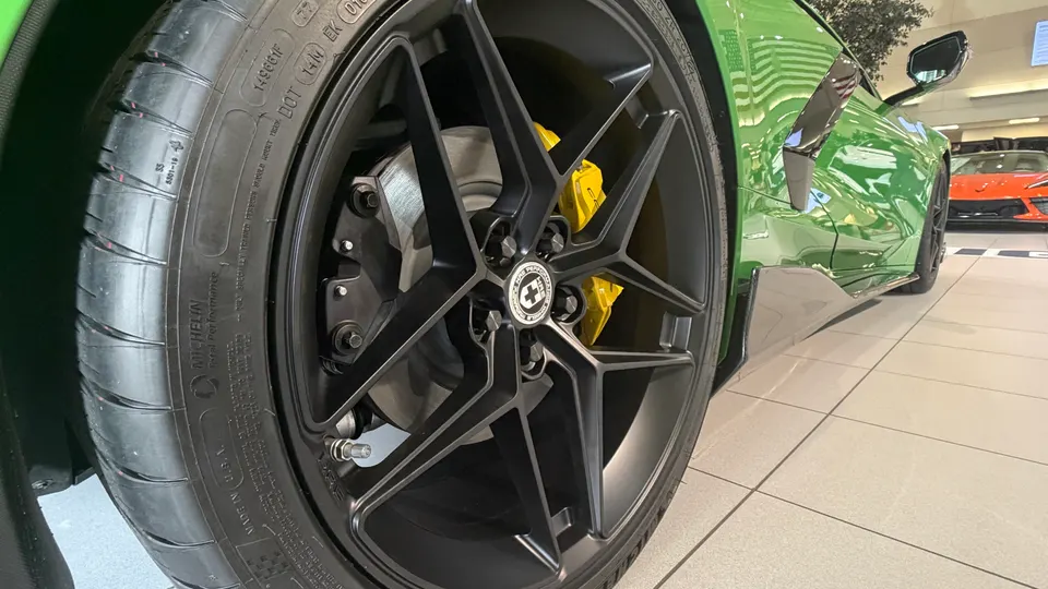 Close-up of a green Corvette C8's custom black HRE wheels with yellow brake calipers and Michelin tires in a showroom.