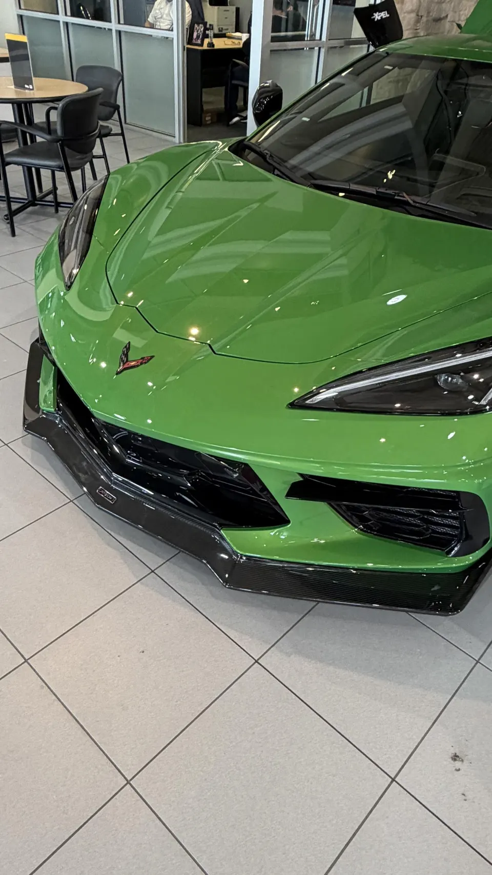 A vibrant green C8 Corvette with a carbon fiber front splitter displayed in a showroom setting.