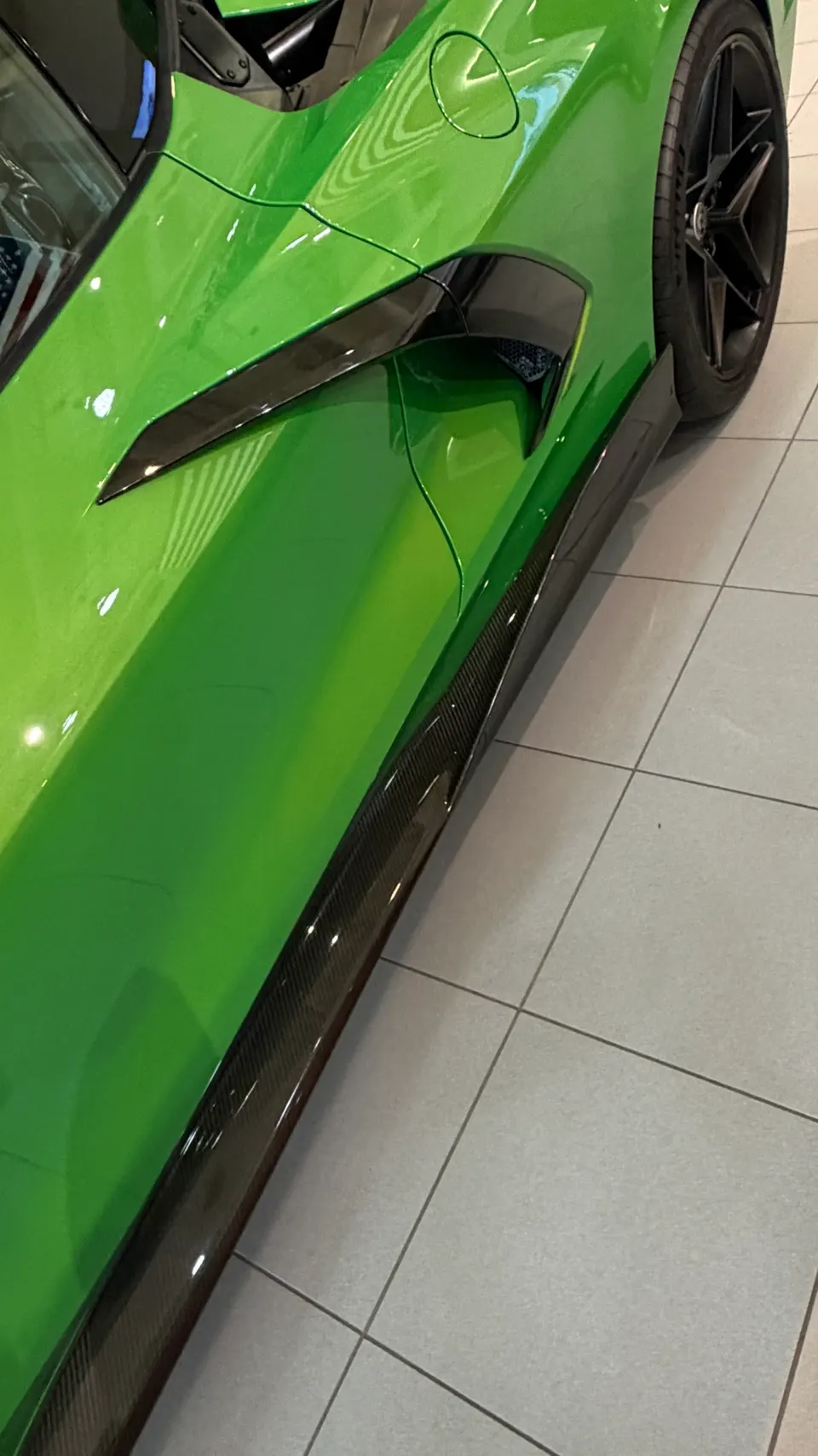 A close-up of a bright green McLaren's side, showcasing its carbon fiber side skirt and aerodynamic air intake.