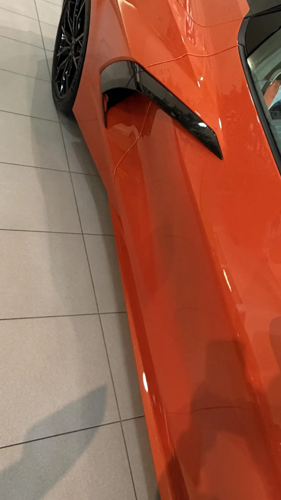 Close-up of the side of an orange Corvette C8, highlighting the black side air intake vent and sleek body lines.