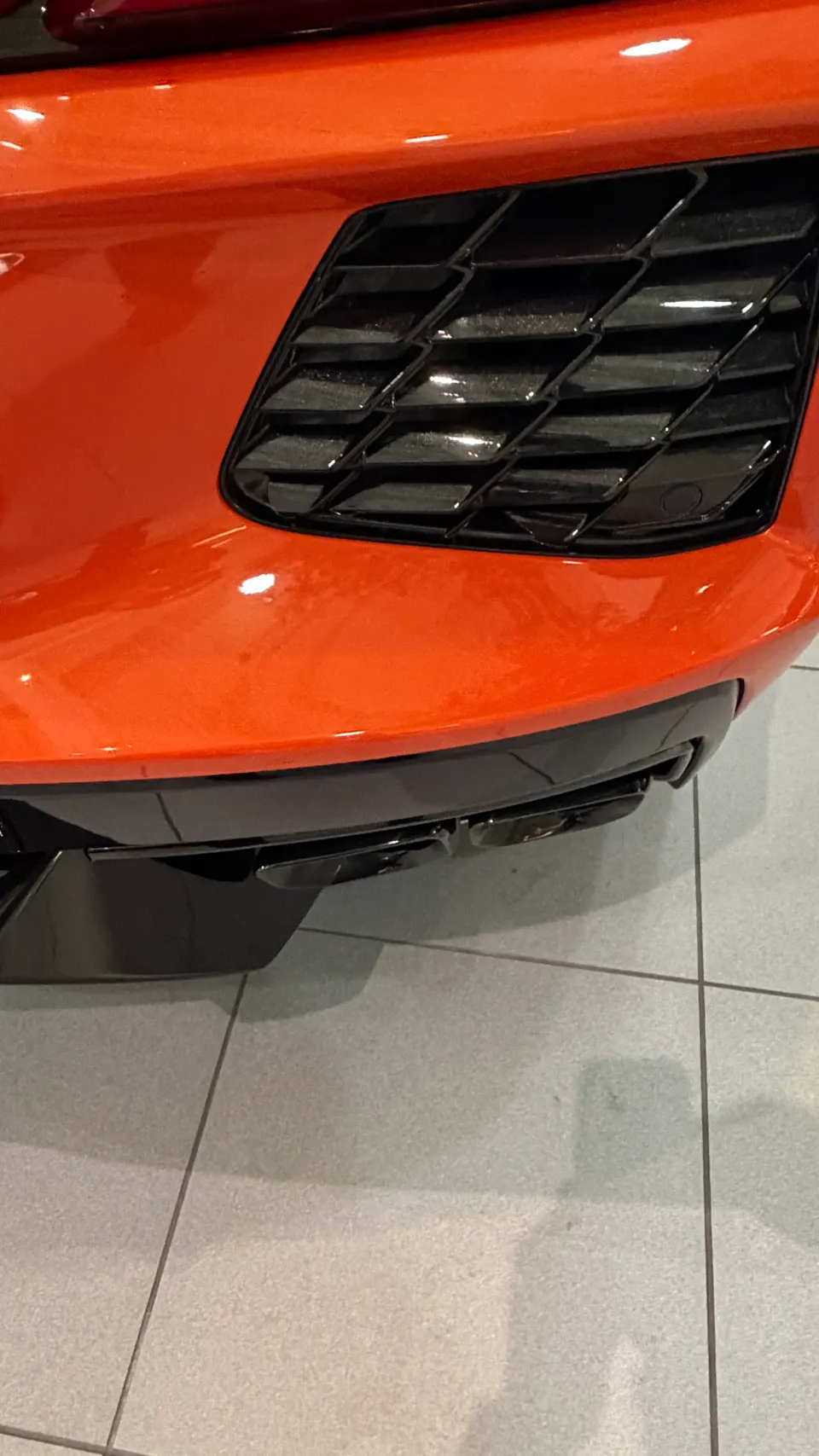 Close-up of the orange front bumper and black grille of a Chevrolet Corvette C8 in a showroom.