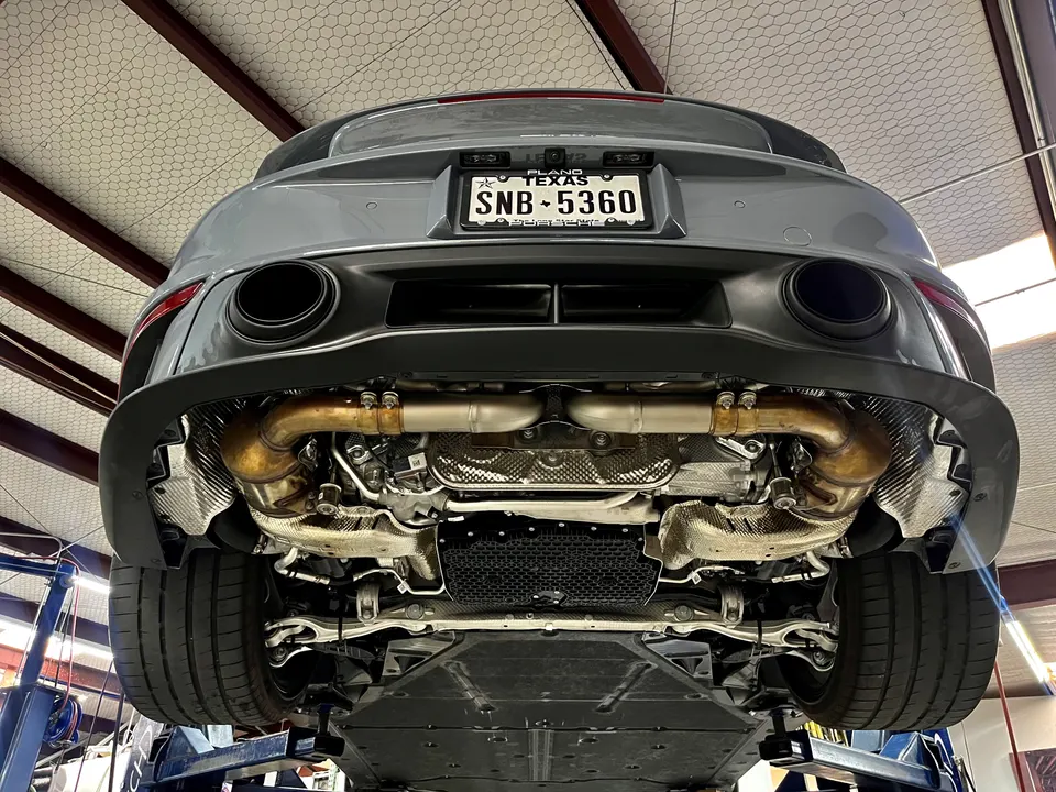 A Porsche sports car on a lift in a shop, showcasing its exhaust system and underside components.