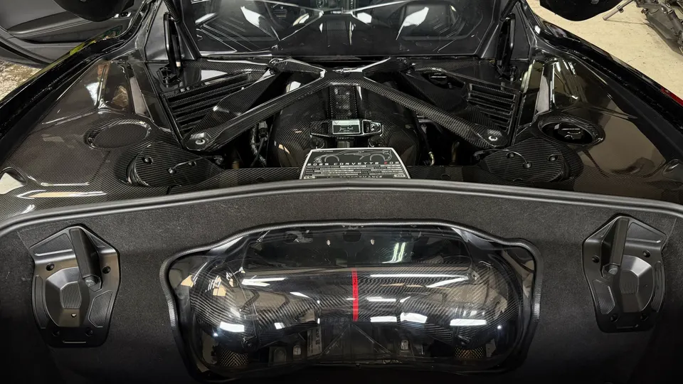 Close-up of a Corvette C8 engine bay featuring carbon fiber engine cover and strut brace, showcasing performance upgrades.