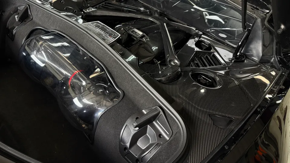 Detailed view of a C8 Corvette engine bay featuring extensive carbon fiber components and an aftermarket intake system.