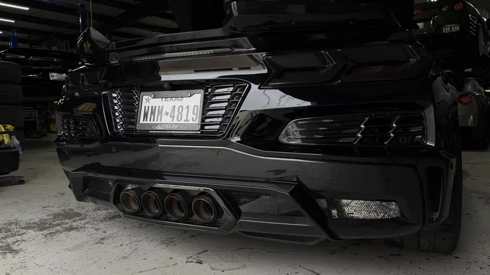 A black C8 Corvette's rear bumper and quad exhaust tips in a Jotech Motorsports shop.