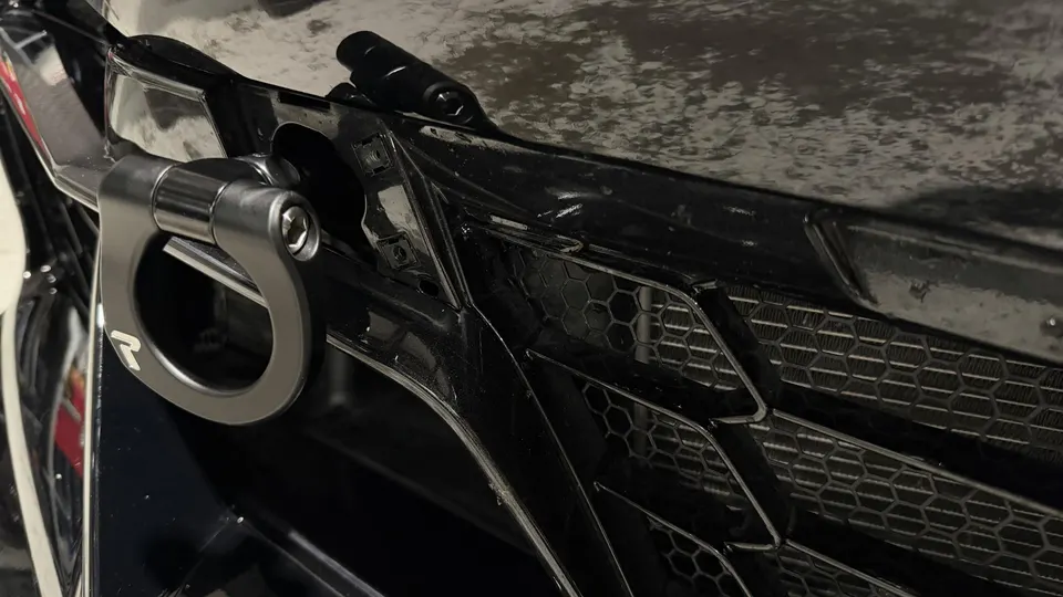 Close-up of a black car's front grille featuring a grey aftermarket tow hook with a logo.