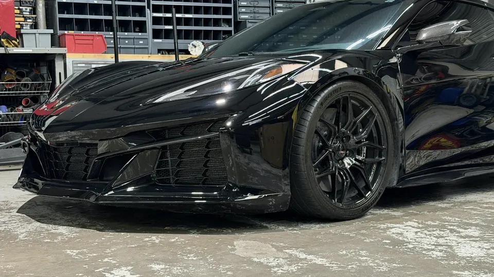A sleek black Chevrolet Corvette C8 with aftermarket wheels parked in a performance tuning shop.