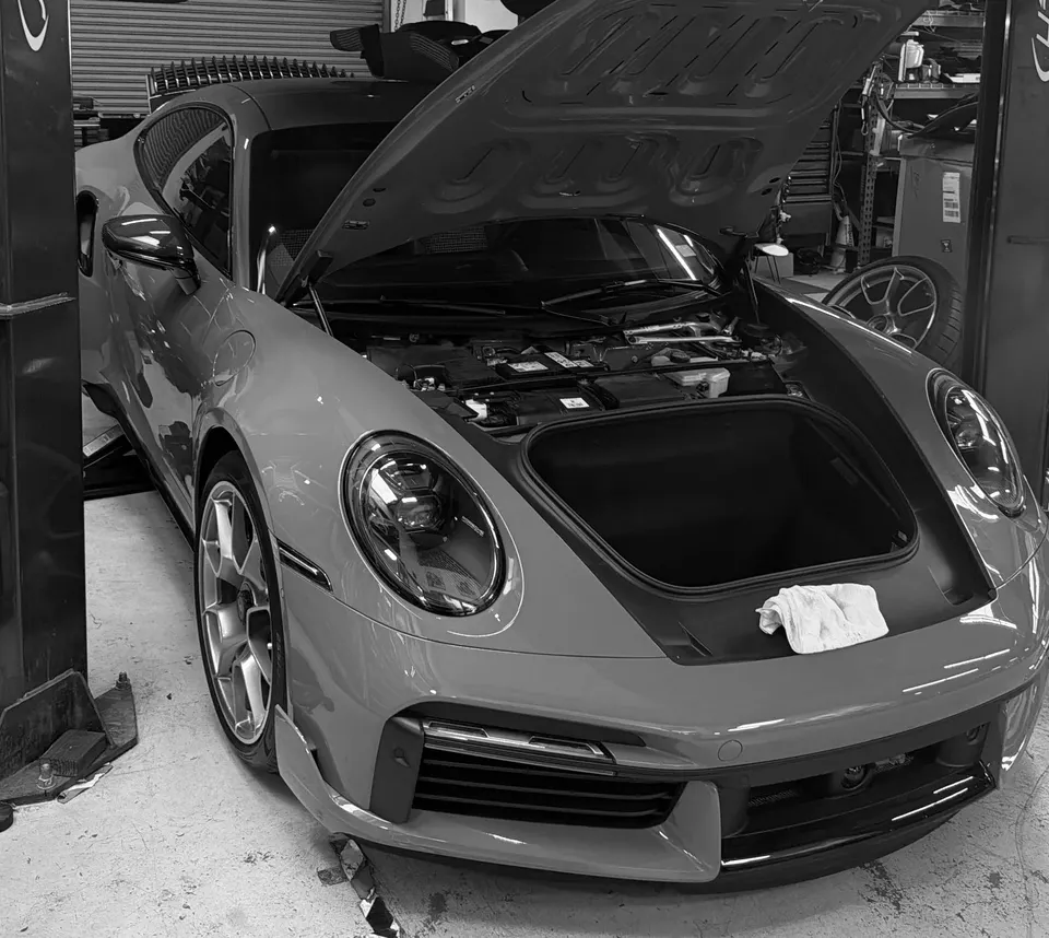 Porsche 911 with its frunk open, on a lift in a performance tuning shop, ready for service or modification.