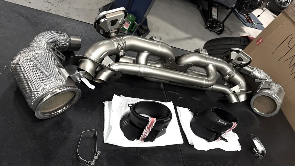 New Akrapovic exhaust system components, including mufflers and piping, laid out on a table in a shop.