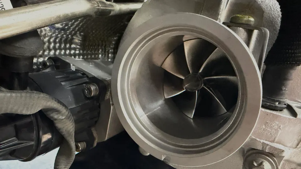 Close-up view of a performance turbocharger's compressor wheel and housing installed in an engine bay.