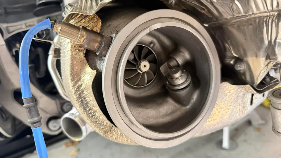 Close-up of a turbocharger with an O2 sensor and heat shield visible in an engine bay.