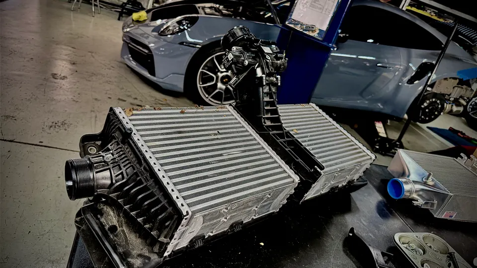 Porsche 911 intercoolers on a workbench in a performance tuning shop, ready for installation.