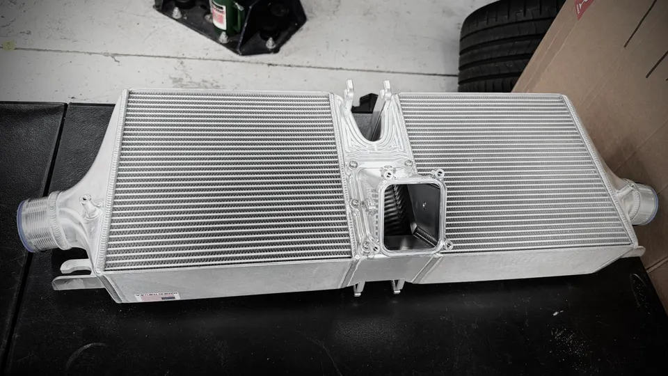 Aluminum performance intercooler on a workbench in a tuning shop, ready for installation.