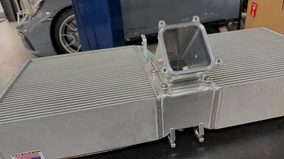 A new performance intercooler for a Porsche, displayed on a surface in a shop setting.