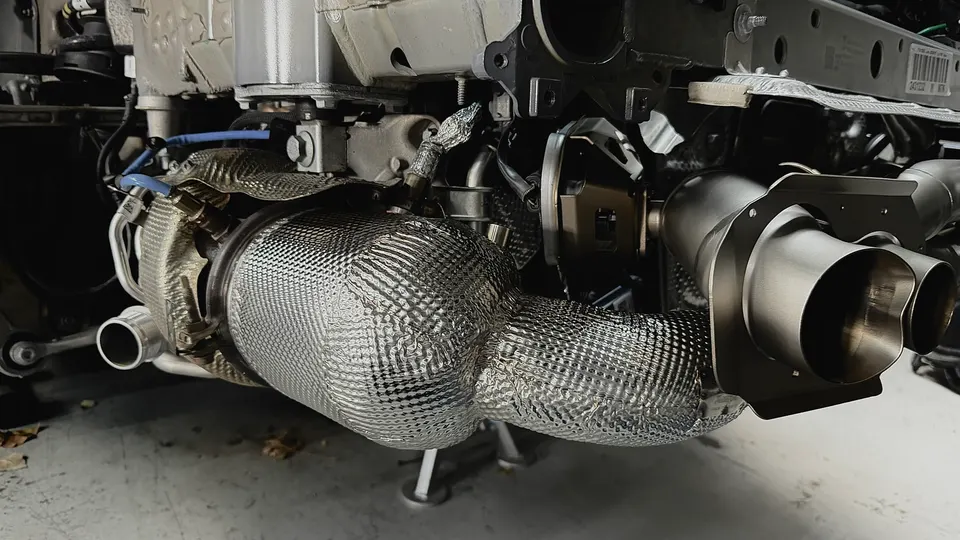 Close-up view of a performance exhaust system with heat shielding and dual exhaust tips on a car underbody.