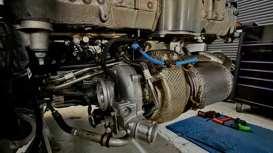 A BMW turbocharger with a heat shield being installed in a performance shop, with tools on the floor.