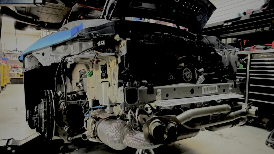 Rear view of a Porsche 911 undergoing an exhaust system installation in a performance tuning shop.