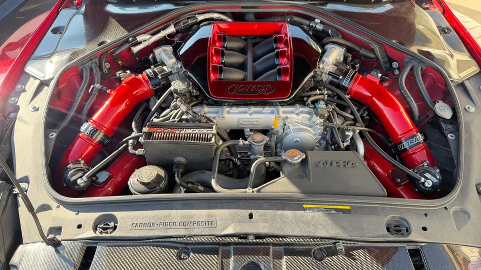 A detailed view of a Jotech-tuned Nissan GT-R engine bay with red intake manifold and boost pipes.
