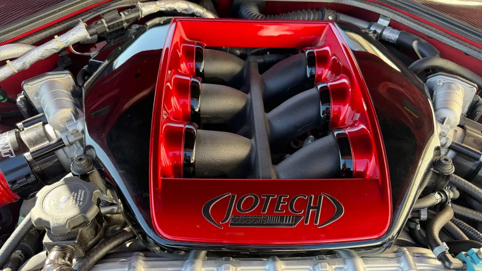 A close-up of a red Jotech Motorsports intake manifold in a car's engine bay, showcasing performance upgrades.