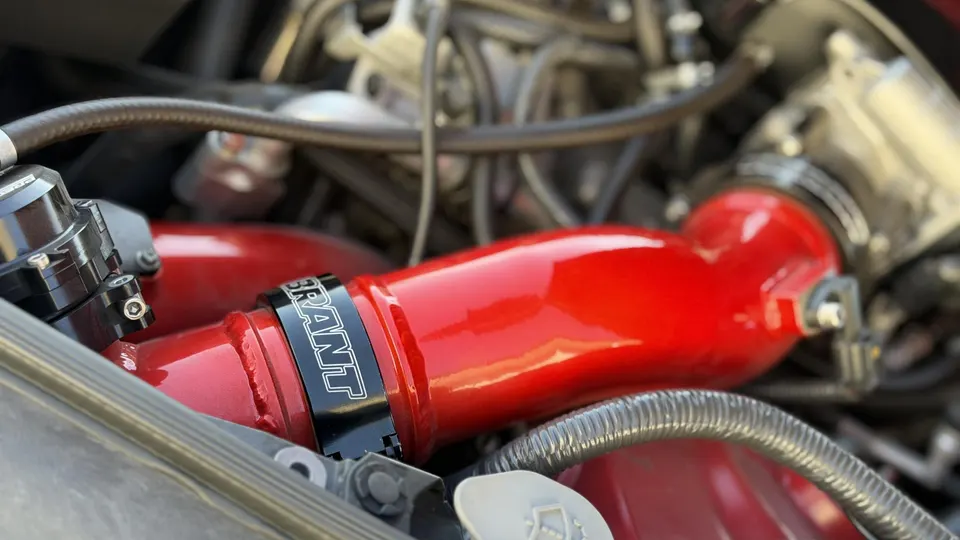 Close-up of a red performance intake pipe and blow-off valve in a car's engine bay, showcasing aftermarket parts.